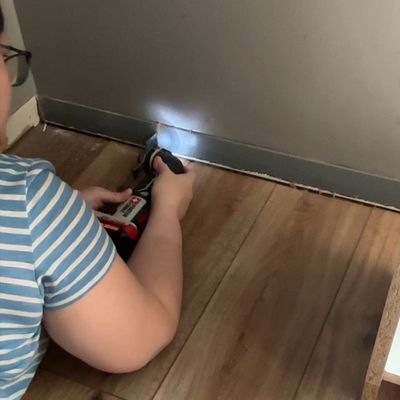 Em holding an oscillating tool against gray baseboard
