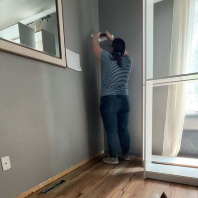 Em standing in the corner of her dining room unscrewing a corner shelf